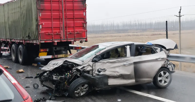 A wrecked car beside a tractor-trailer on a wet highway after a collision, with debris scattered across the road