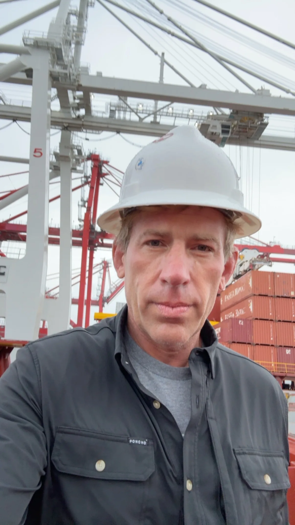 Brian Beckcom inspecting a vessel at a container terminal, ship-to-shore cranes and stacked containers behind