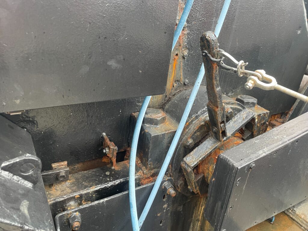 Close-up of black winch components, metal linkage and blue hoses.