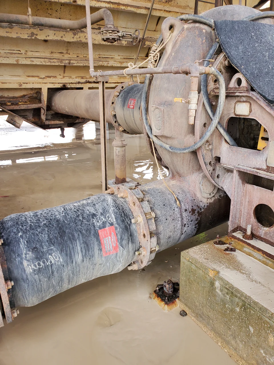 Large pipe connections beside industrial equipment and standing water.