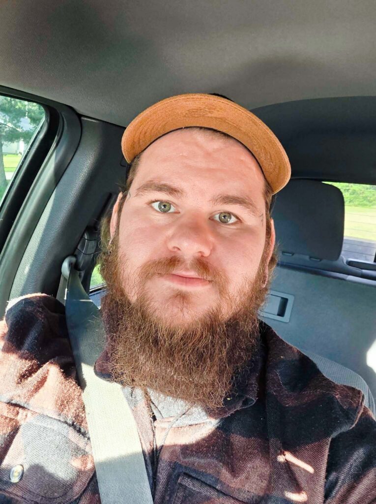 Our client seated in a vehicle, wearing a cap and plaid shirt.