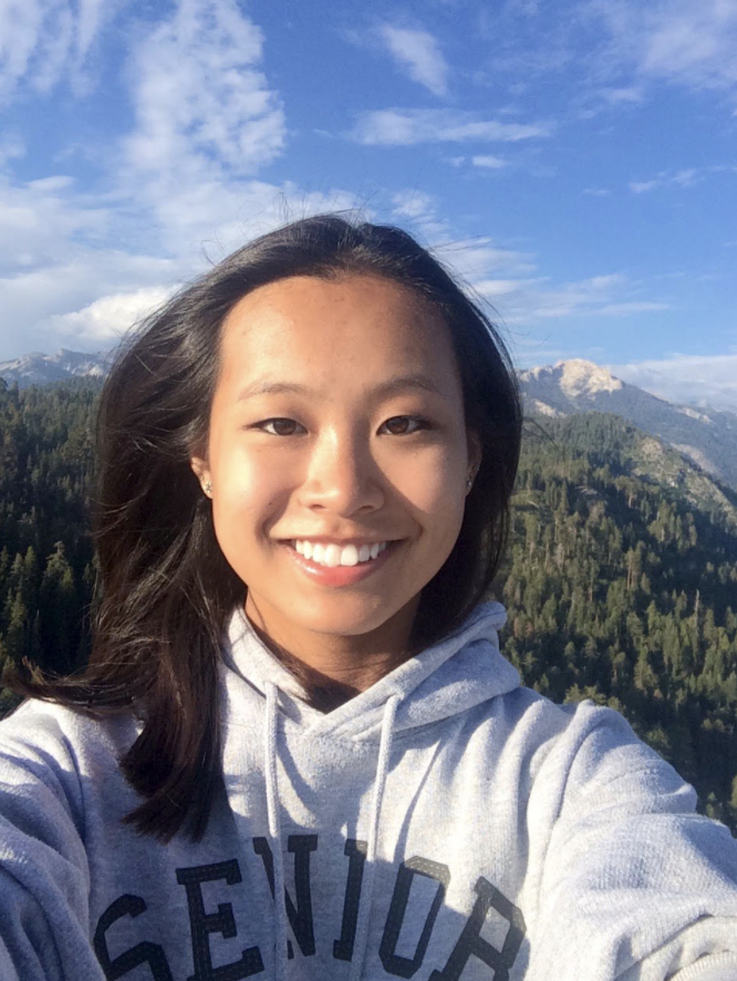 Audrey smiling outdoors with mountains and trees behind her.