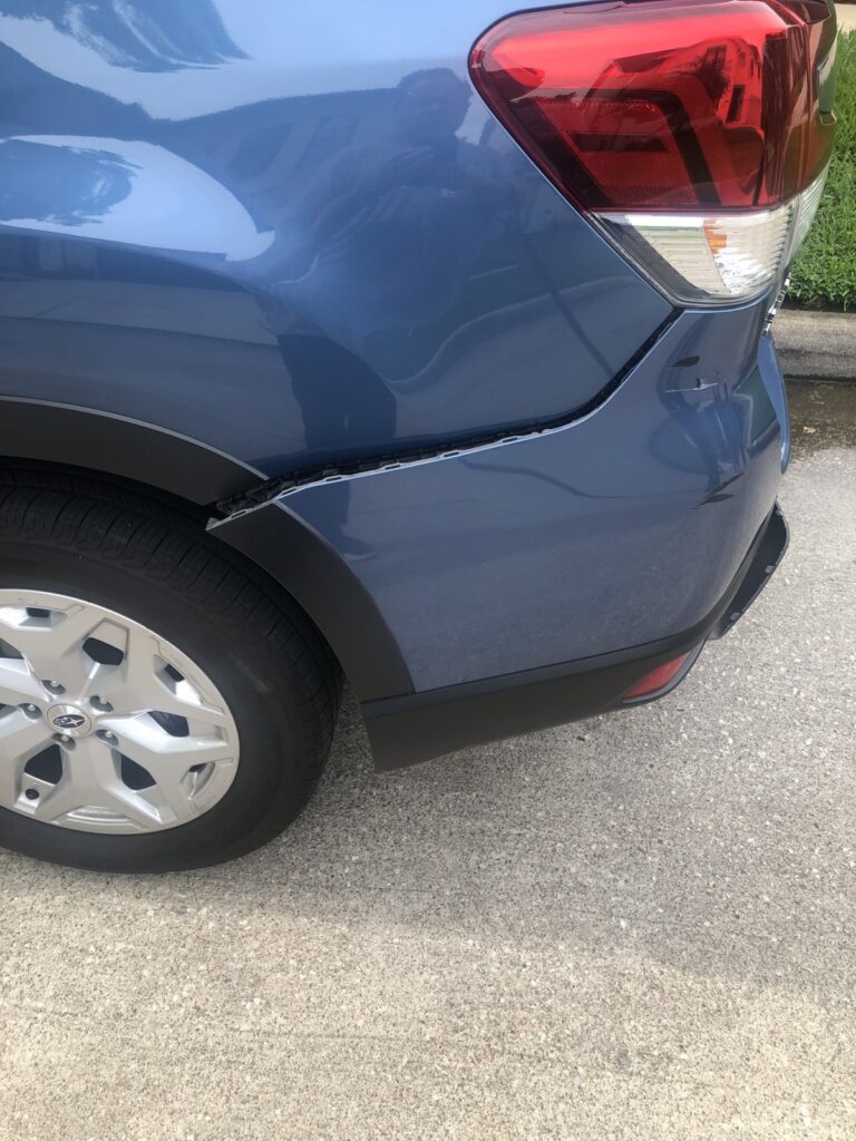 Blue Subaru with a separated rear bumper panel below the left taillight.