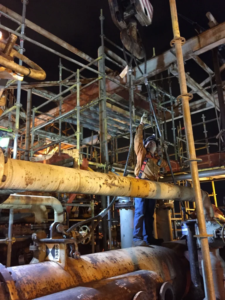 Worker beside pipework, scaffolding, and suspended rigging at ExxonMobil’s Beaumont refinery.