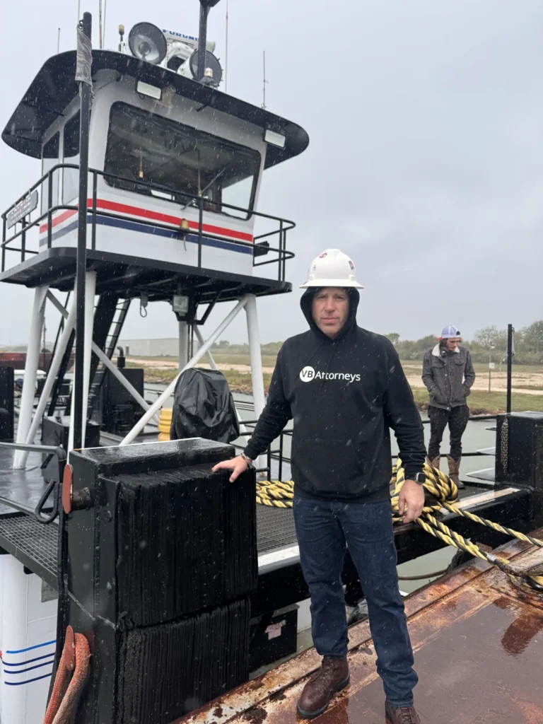 Brian Beckcom in a hard hat on a wet barge deck beside a towboat.