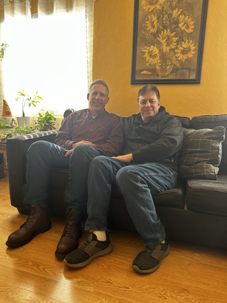 Brian Beckcom and Harvey S. seated together on a sofa.