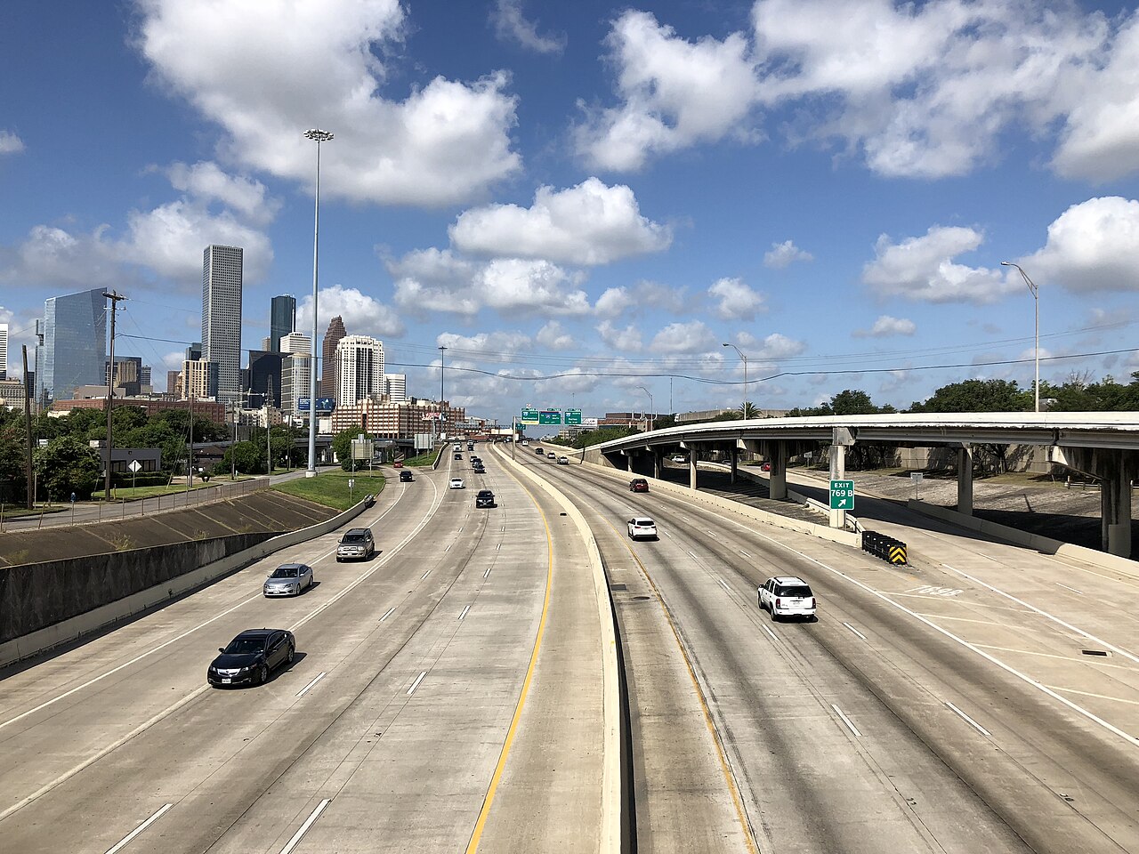 Traffic on Interstate 10 in Houston with downtown buildings to the left and an elevated ramp to the right.