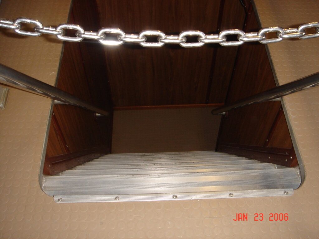 View down a narrow stairwell with handrails on both sides and a chain across the opening.