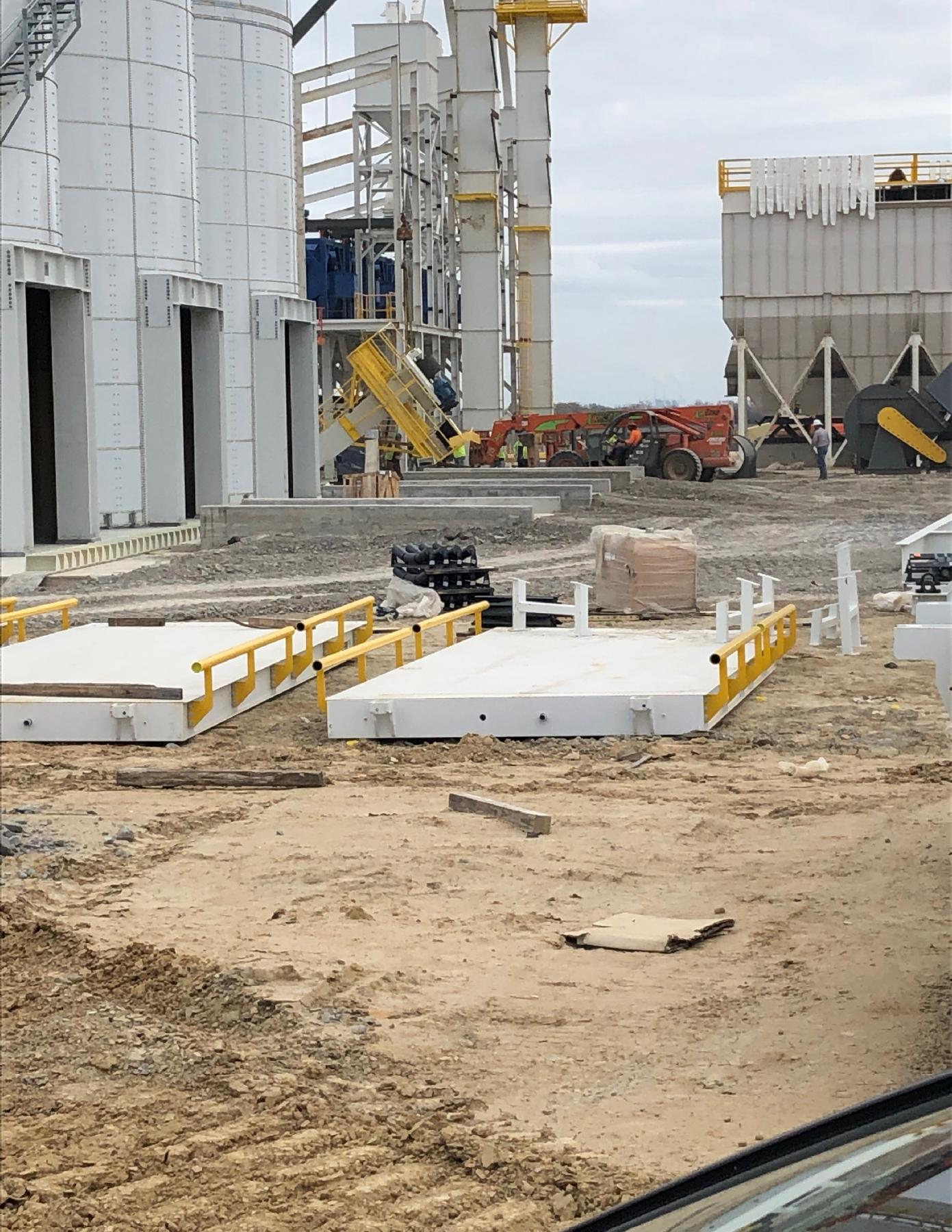 Industrial construction site with a tilted yellow-railed platform near a bucket elevator