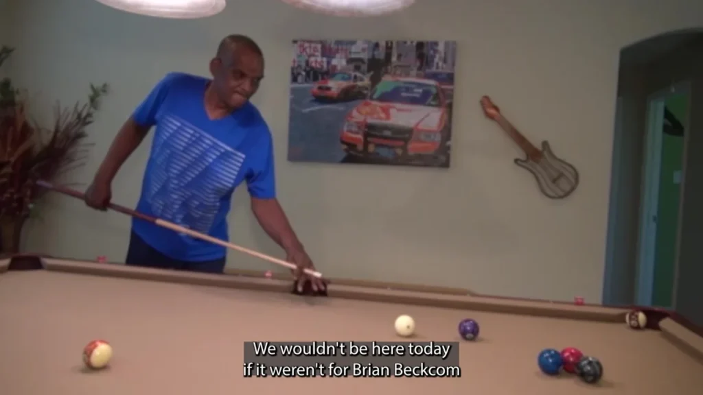 Johnny Harris leaning over a pool table with a cue at home.