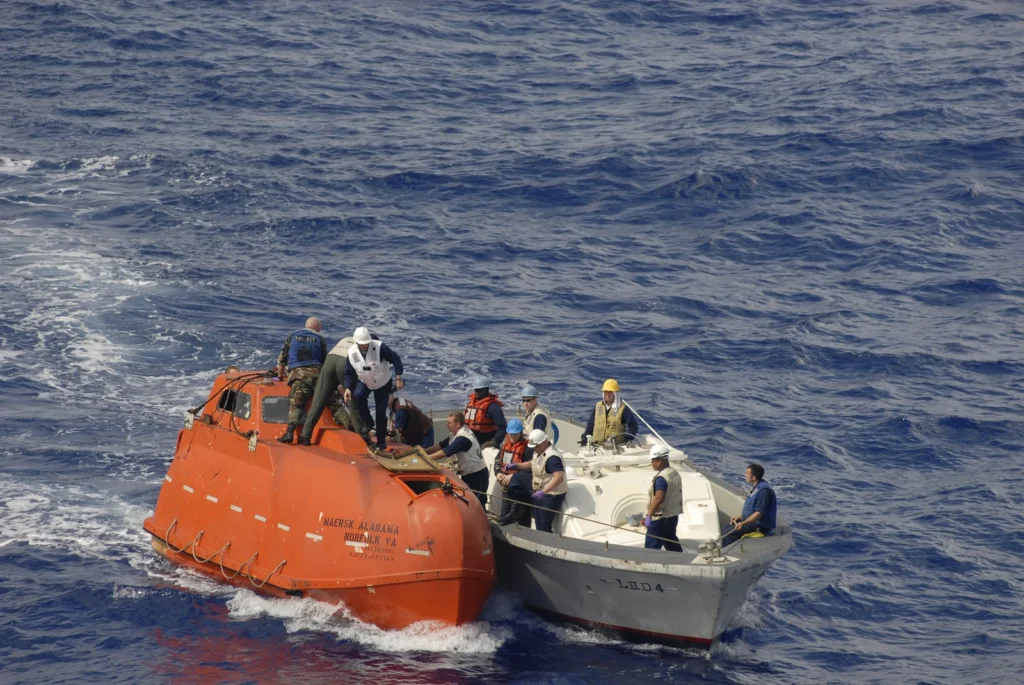 A USS Boxer team alongside the orange Maersk Alabama lifeboat during post-rescue towing for evidence processing.