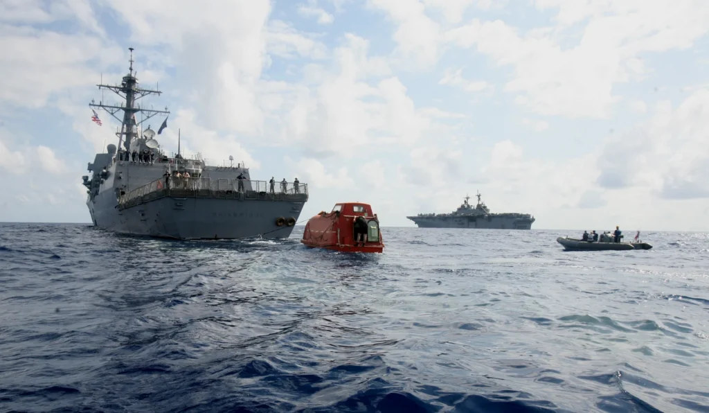 USS Bainbridge tows the Maersk Alabama lifeboat toward USS Boxer, visible farther away.