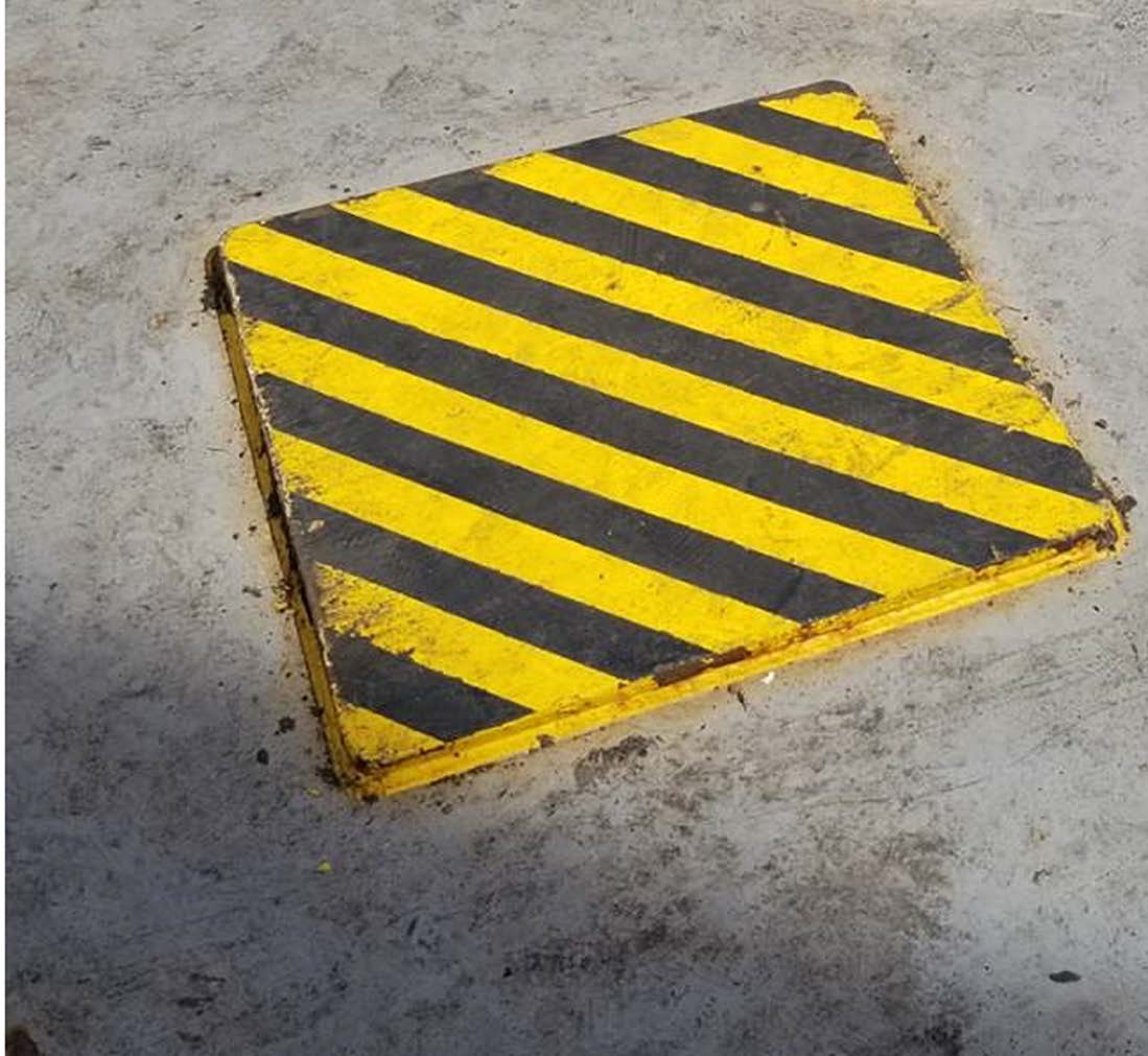 Raised steel doubler plate painted with yellow-and-black diagonal stripes on a vessel deck.