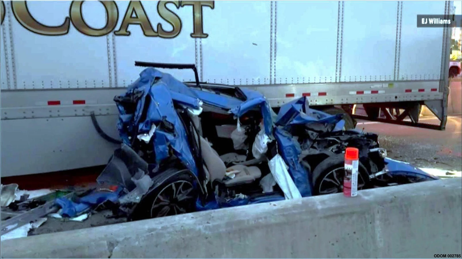 Rogers I-10 collision: blue BMW beside GoldCoast trailer Severely damaged blue BMW beside a GoldCoast trailer and concrete barrier at the Rogers Interstate 10 crash scene.