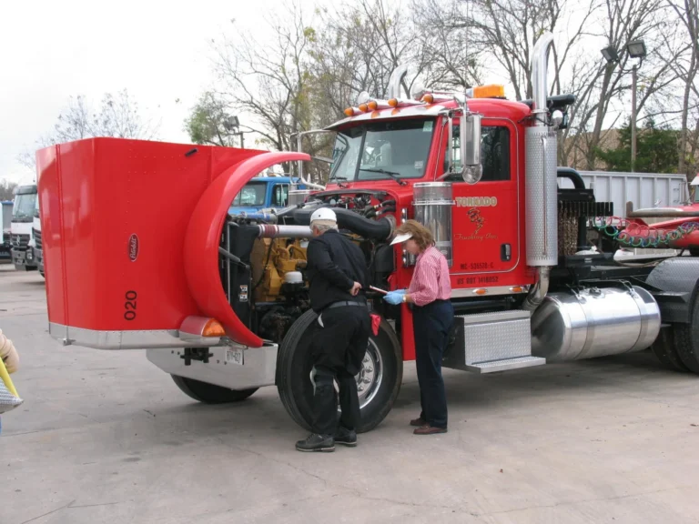 Two people examine a red Tornado Trucking tractor with its hood open and engine exposed.
