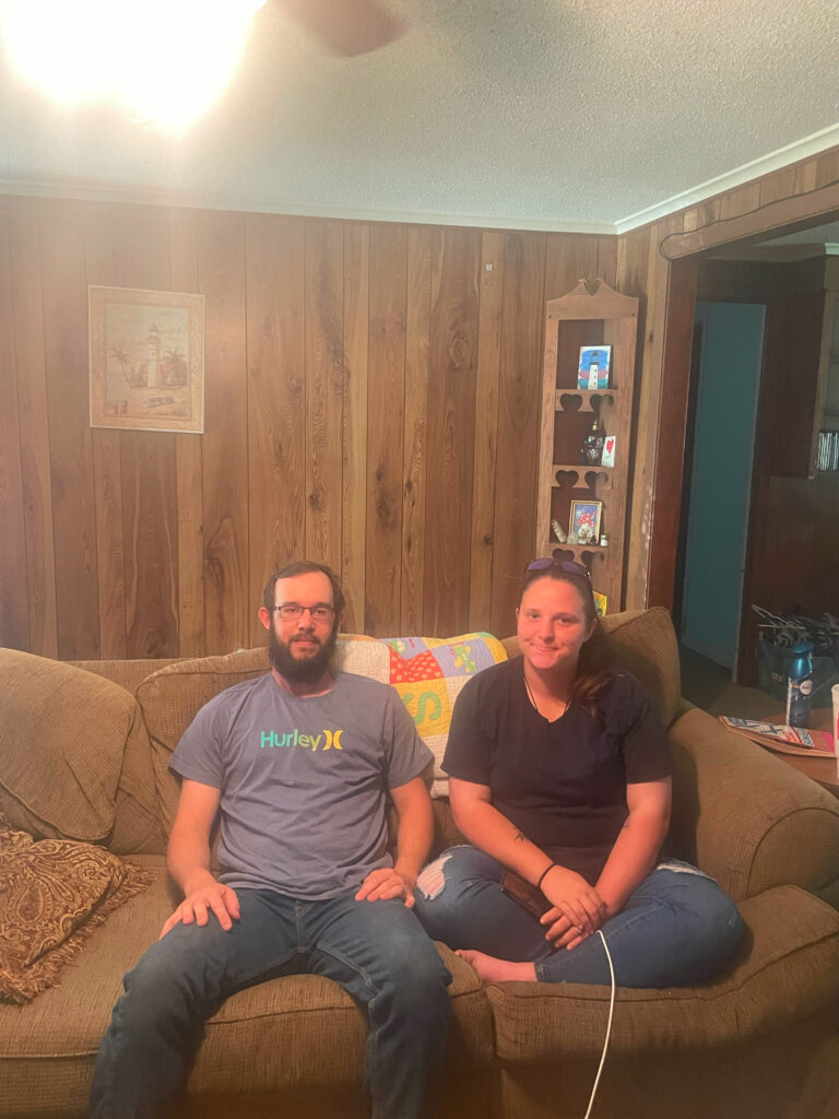 Trenton B., a deckhand, seated on a couch with his wife.