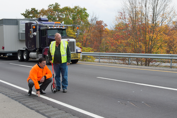 Vuk Vujasinovic in an orange jacket examines pavement markings alongside an accident reconstruction expert.